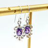 Silver earrings with amethyst gemstones on an earring stand on a white background