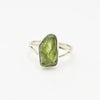 Silver ring with a raw green peridot stone on a white background