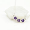Silver necklace with three purple amethyst gemstones on a white background