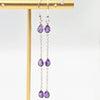 Purple teardrop earrings on a gold earring stand against a white background